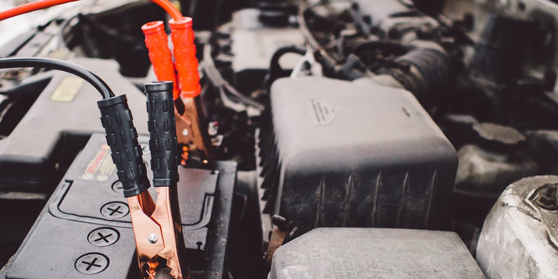 Car battery under the hood with jump-start cables connected, showing a detailed view of engine components, dreaming of Christmas.